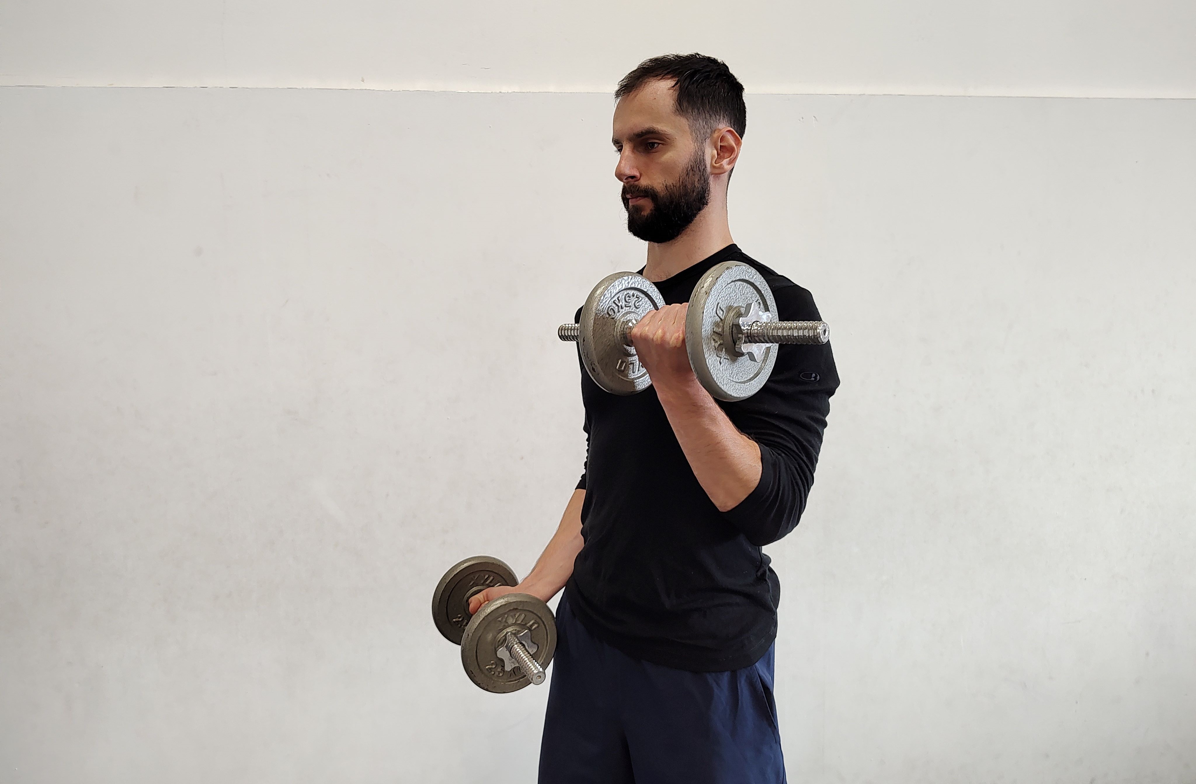 Muž v tělocvičně cvičí bicepsový zdvih s jednoručkami.